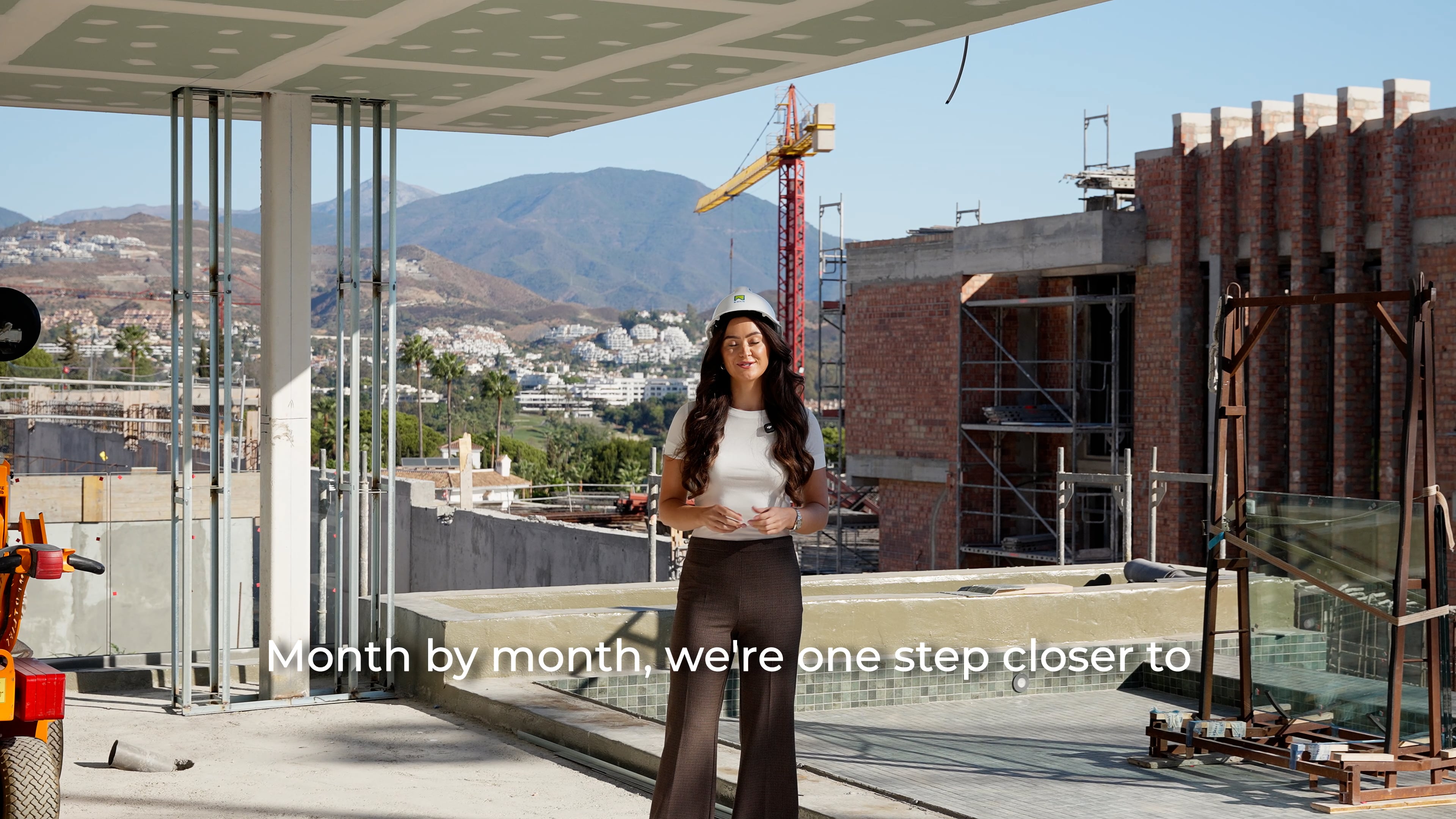 Woman in a hard hat stands on a Marbella construction site with mountains and buildings behind