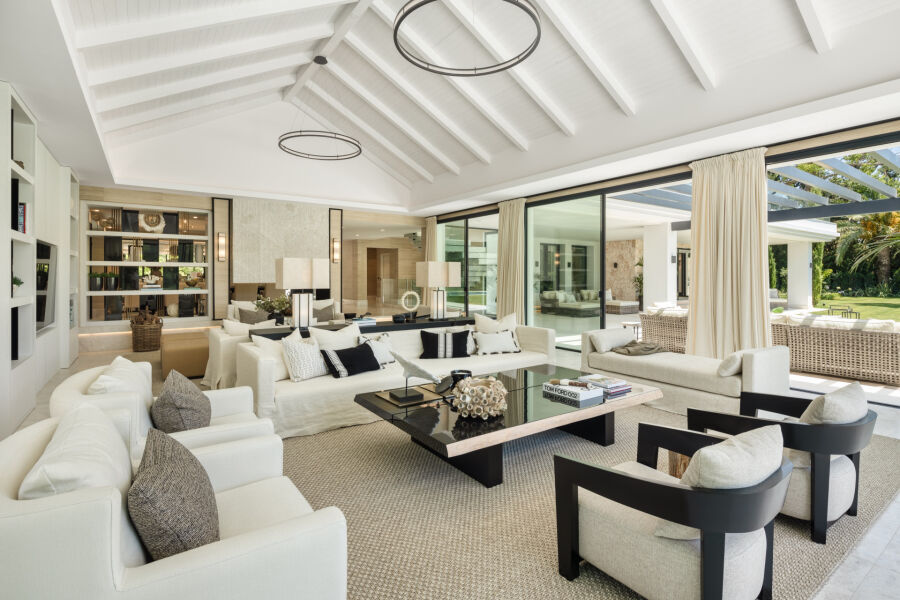 Salón abierto en una villa de Marbella con sofás blancos, mesa de centro de cristal y puertas correderas a la terraza