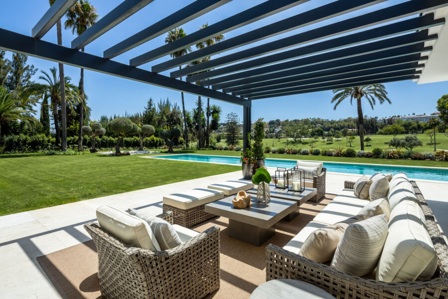 Terraza con pérgola, sofás de mimbre, piscina y vistas al campo de golf en una villa de Marbella