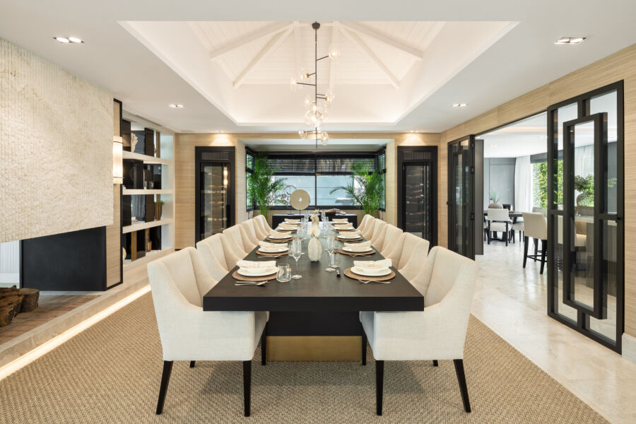 Comedor de una villa en Marbella con mesa larga, sillas crema, chimenea y puertas abiertas a otra estancia