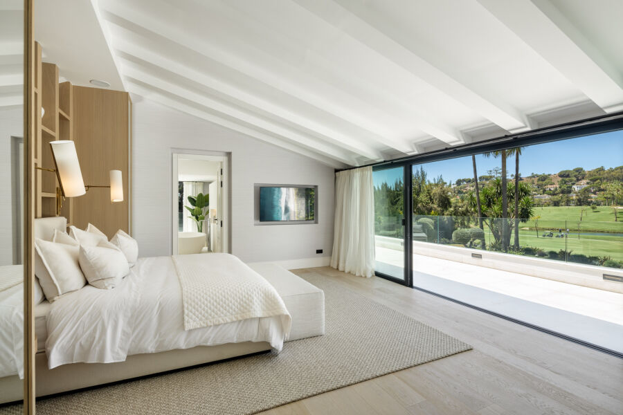Dormitorio en una villa de Las Brisas con techo inclinado blanco y puertas correderas a vistas al golf