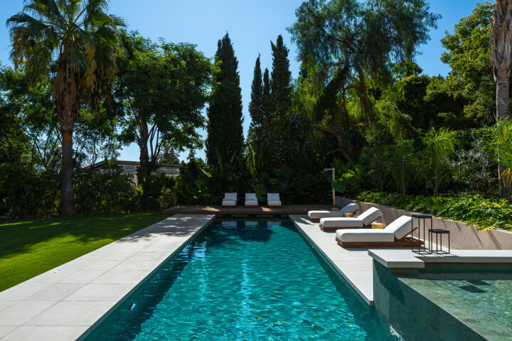 Piscine de la villa bordée de dallage blanc, de chaises longues et de palmiers luxuriants à Nueva Andalucia, Marbella