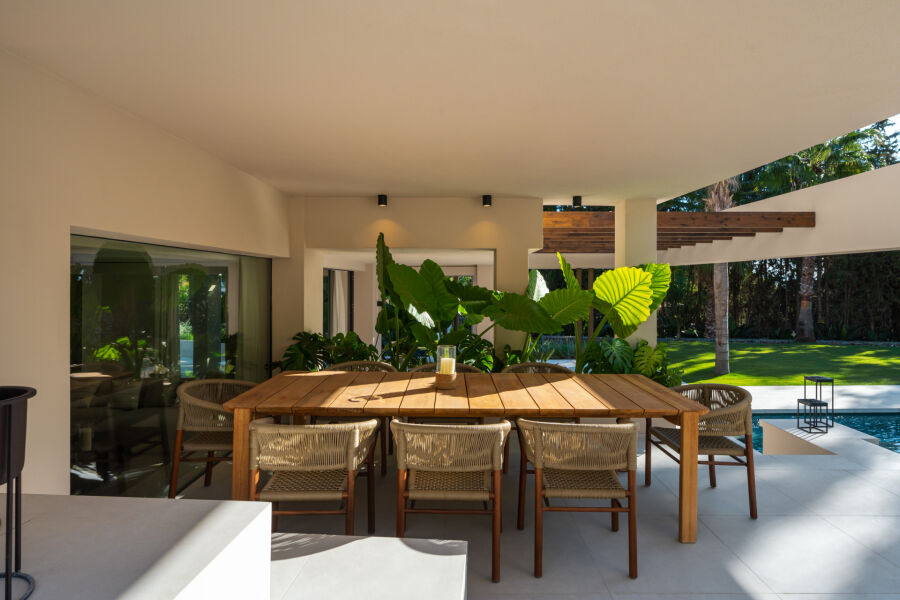 Covered terrace at a villa in Nueva Andalucia with wooden dining table, woven chairs and poolside garden view