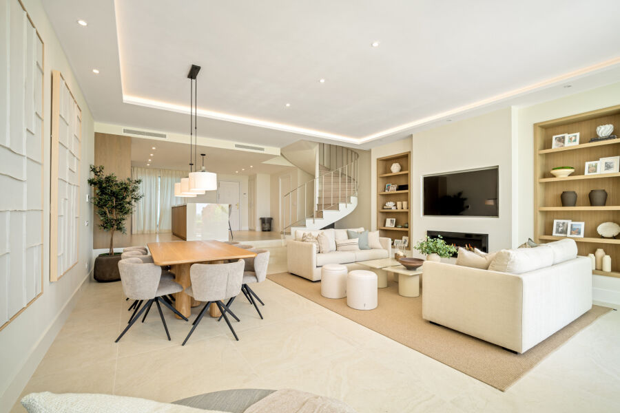 Salón y comedor diáfanos en una casa adosada en La Quinta con sofás, TV, escalera y estanterías de madera