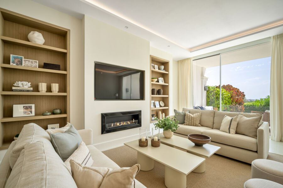 Salón de townhouse en La Quinta con sofás beige, estanterías empotradas, chimenea mural y salida al jardín