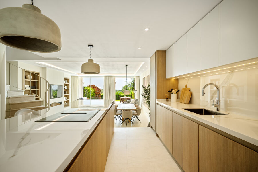 Cocina y comedor de planta abierta en una casa adosada de La Quinta, con muebles de madera, encimeras blancas y vistas al jar