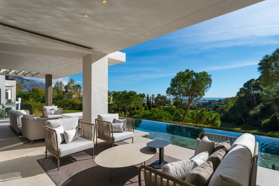 Covered terrace at a villa in La Quinta, Benahavis with seating by an infinity pool and garden views