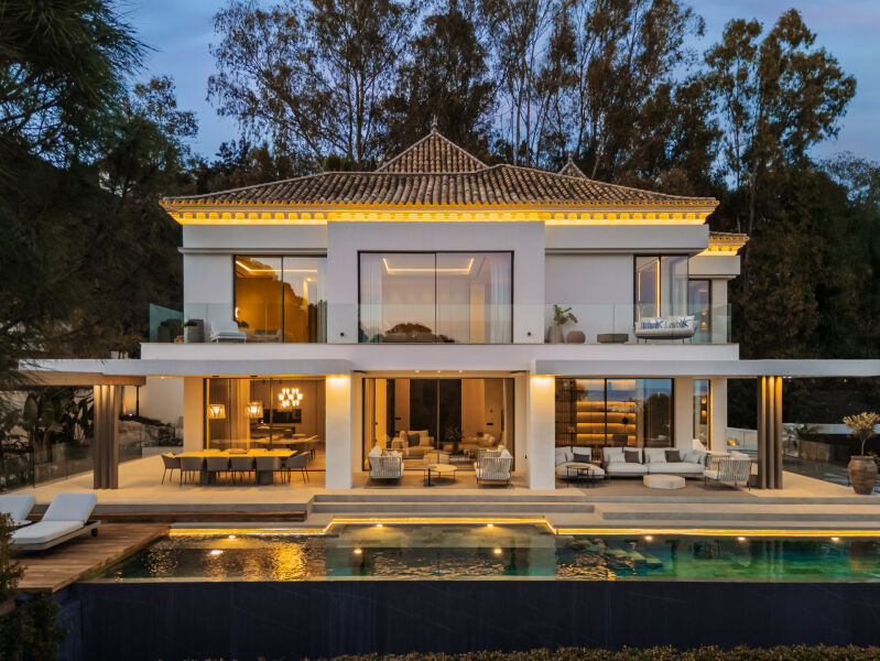 La Quinta villa at dusk with lit terraces, large glass doors and a pool in front
