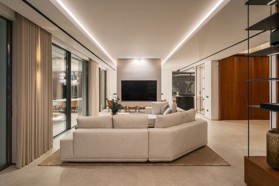 Open-plan villa living room in La Quinta, Benahavis with beige sectional sofa, wall-mounted TV and floor-to-ceiling sliding d