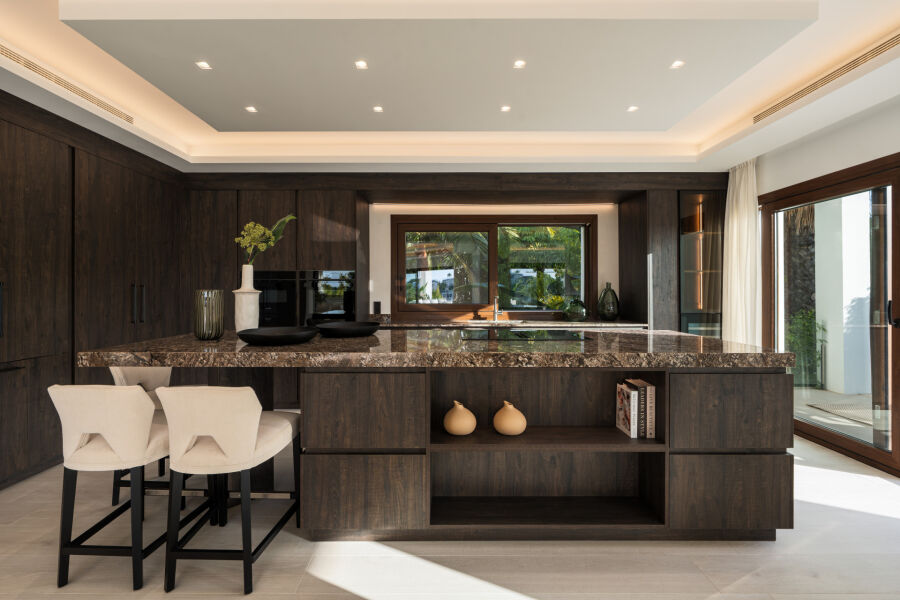 Îlot de cuisine avec plan en pierre, meubles en bois foncé et deux tabourets à Villa Aura, El Herrojo