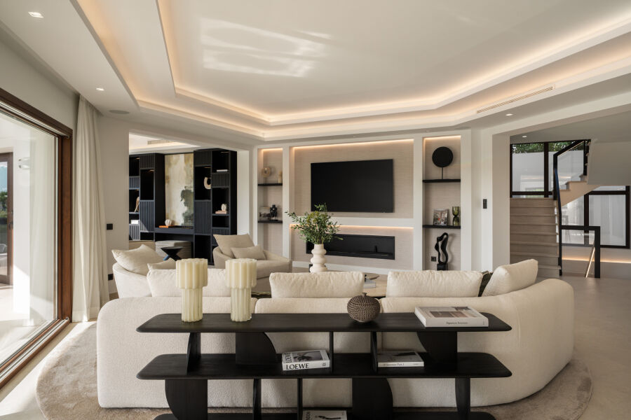 Salon ouvert dans une villa à Benahavis avec canapés beiges, TV murale et éclairage encastré