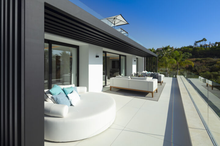 Terrace with white outdoor seating and glass railing at a villa in Nueva Andalucia, Marbella