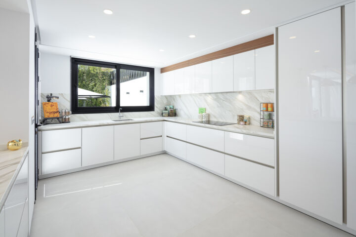 White villa kitchen in Nueva Andalucia with marble splashback, black-framed window and glossy cabinetry
