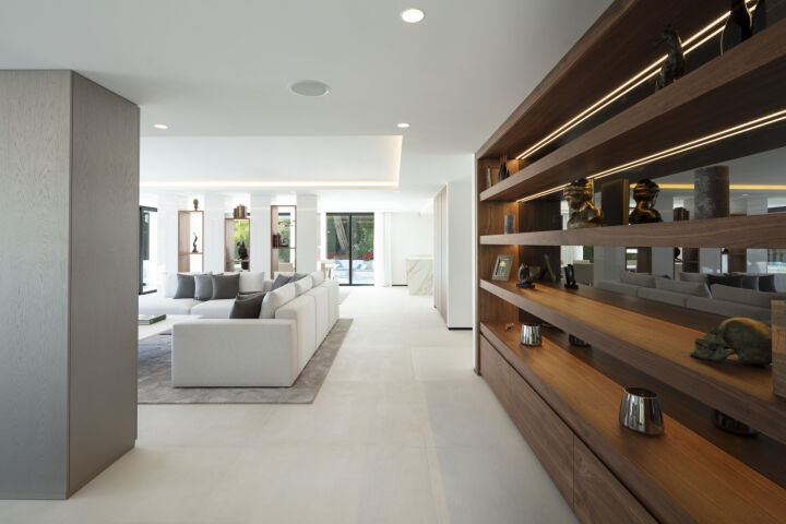 Open-plan living area in a Nueva Andalucia villa with white sofas, wood shelving and sliding doors to the terrace