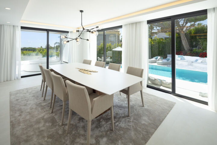 Dining area in a Marbella villa with a white table, beige chairs and floor-to-ceiling windows to the pool and garden